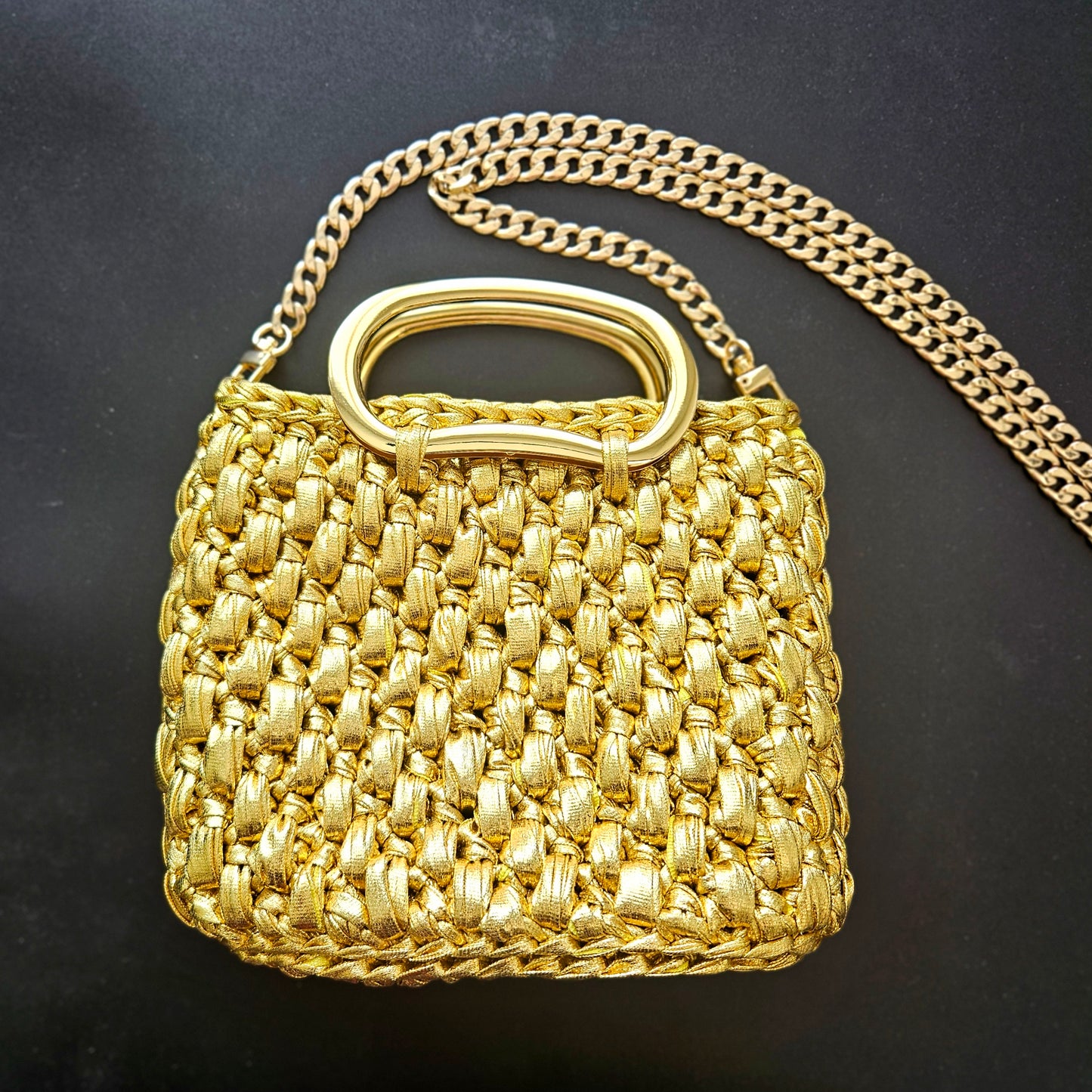 Gold crochet handbag with a chain strap on a black background