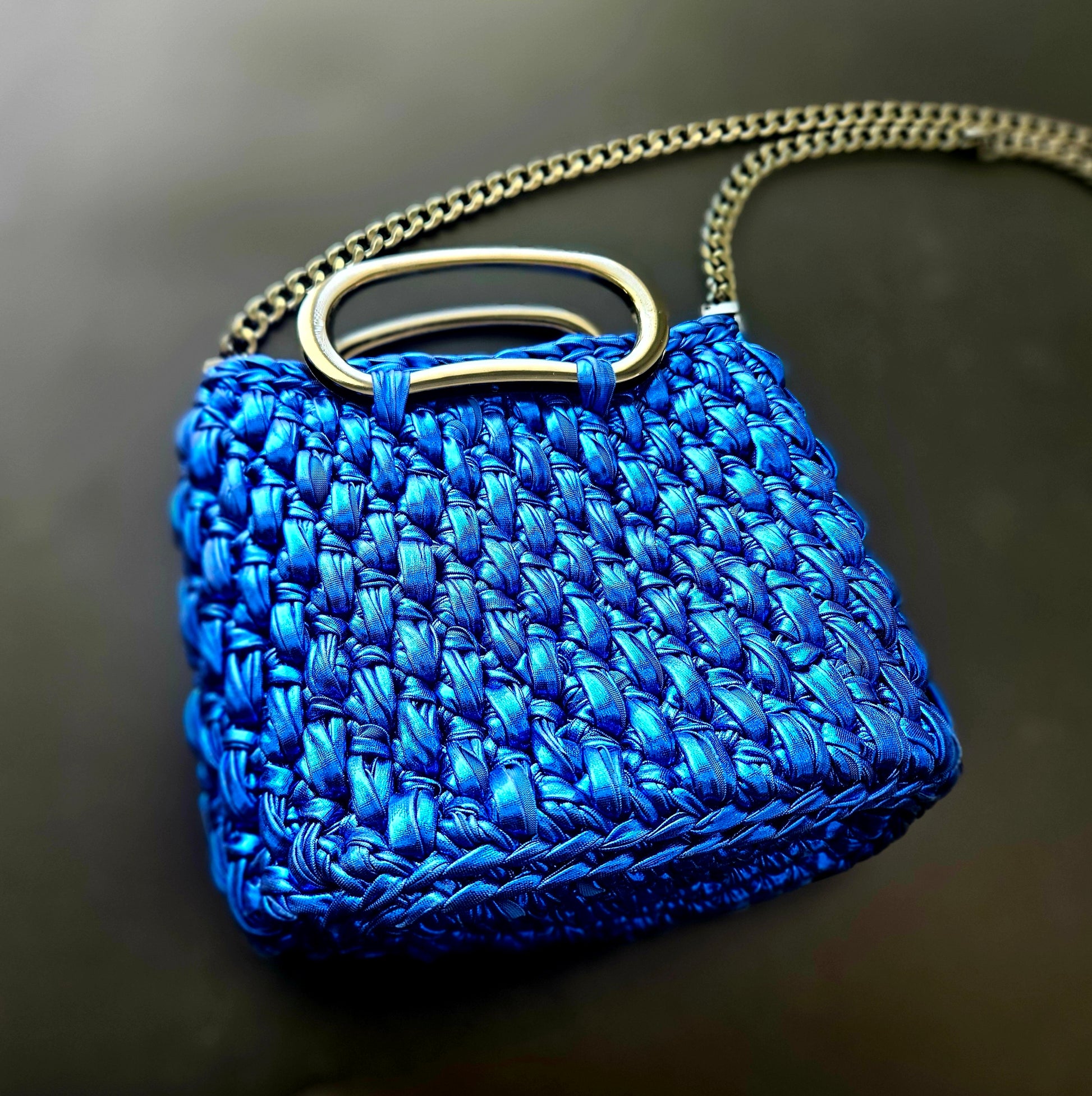 Blue crochet handbag with a gold handle on a dark background