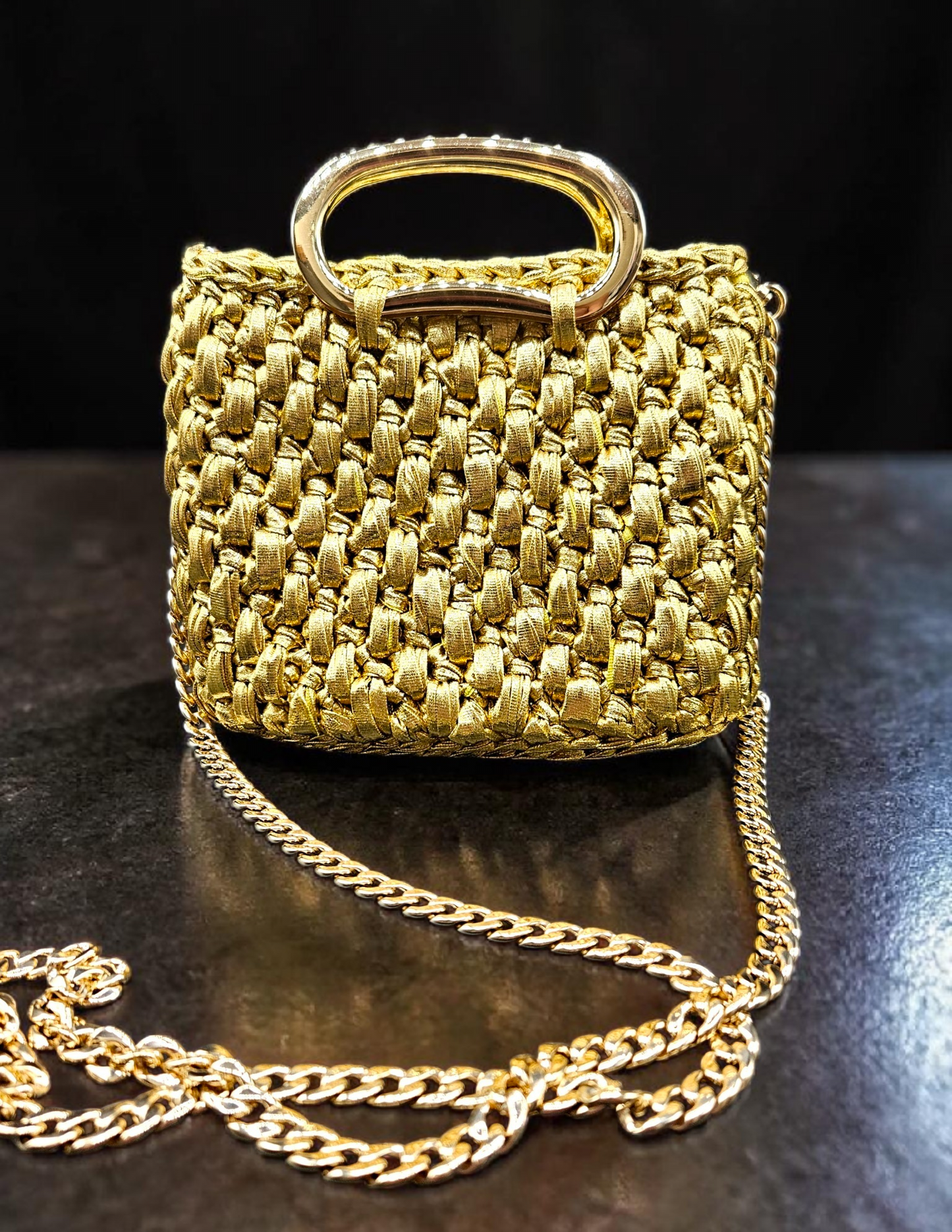 Gold crochet handbag with chain strap on a dark surface