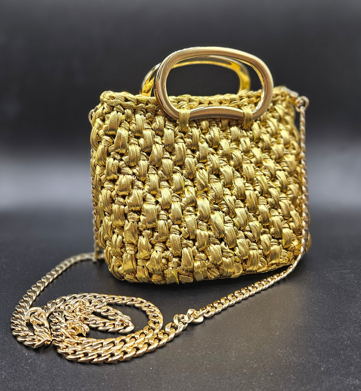 Gold crochet handbag with a chain strap on a dark background