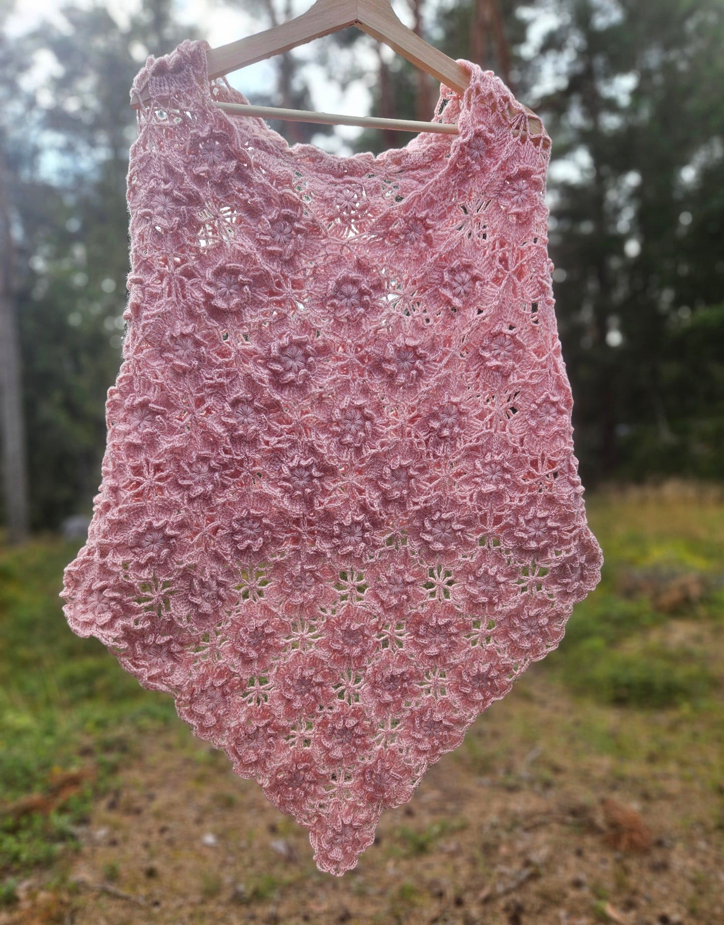 Pink crochet sakura poncho on a hanger against a natural background
