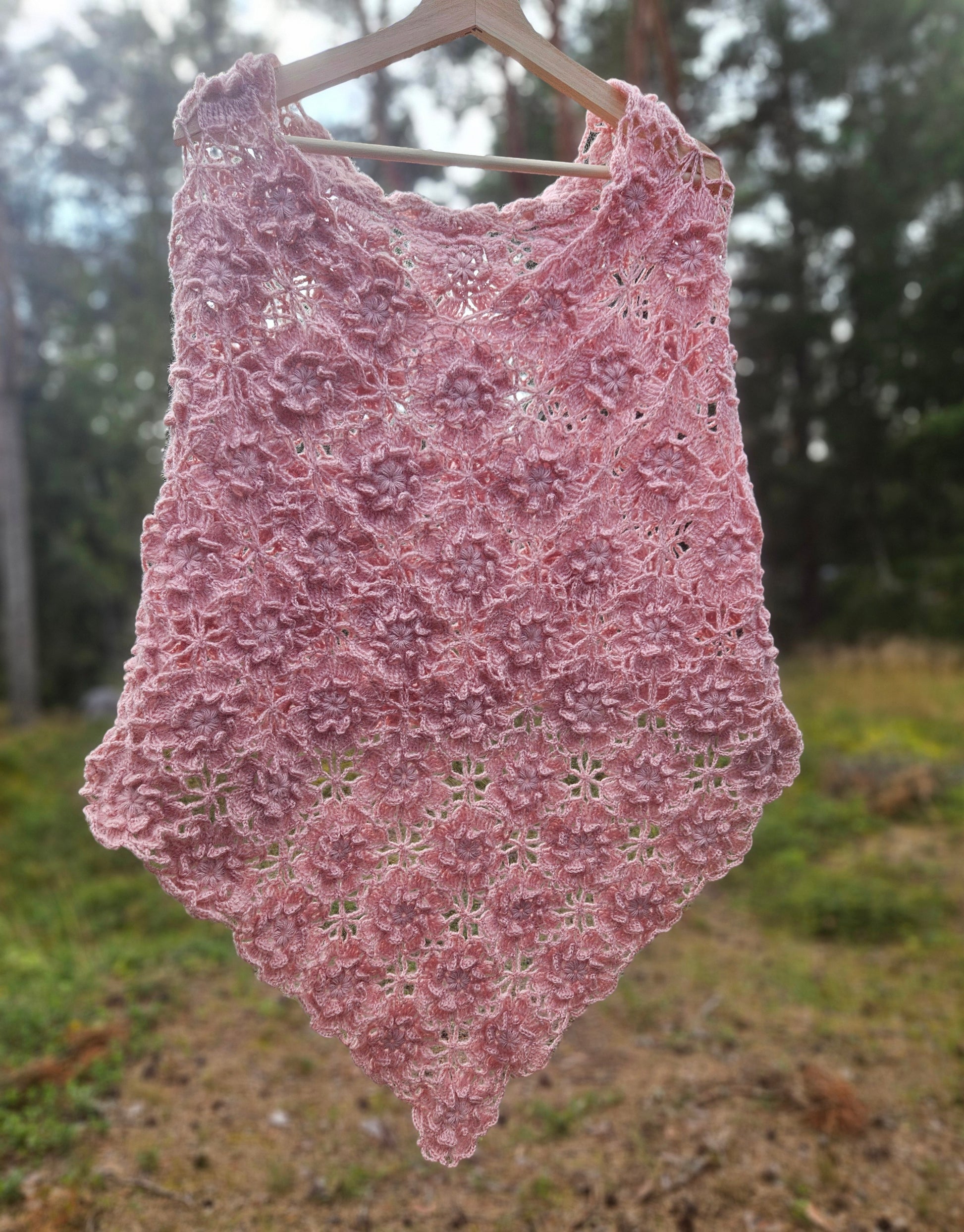 Pink crochet sakura poncho on a hanger against a natural background