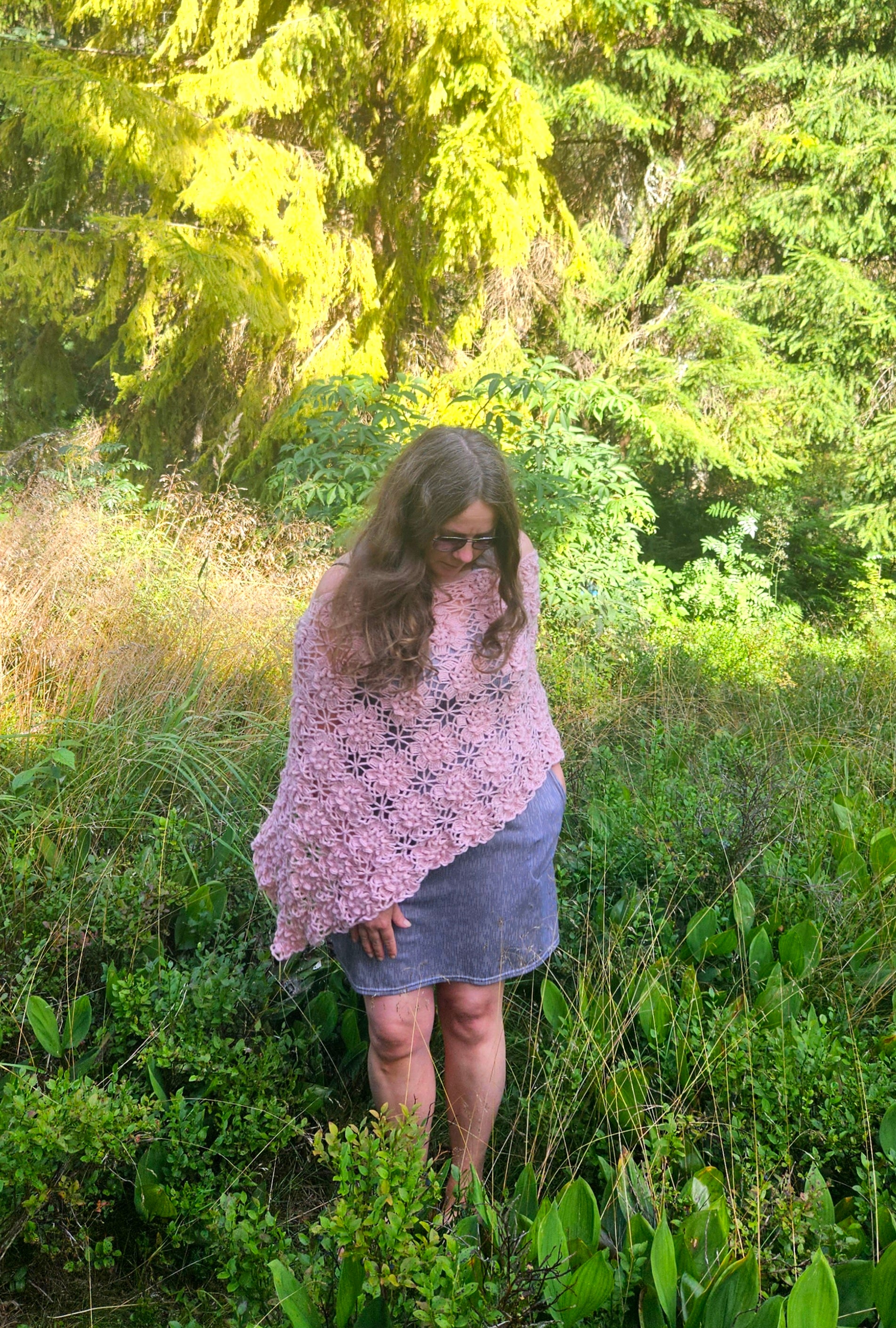 Woman wearing a pink crochet sakura poncho in a forest setting