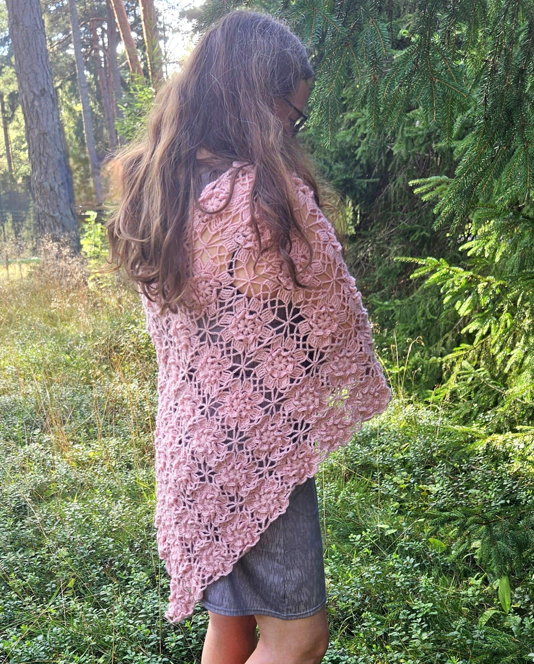 Woman wearing a pink crochet sakura poncho in a forest setting