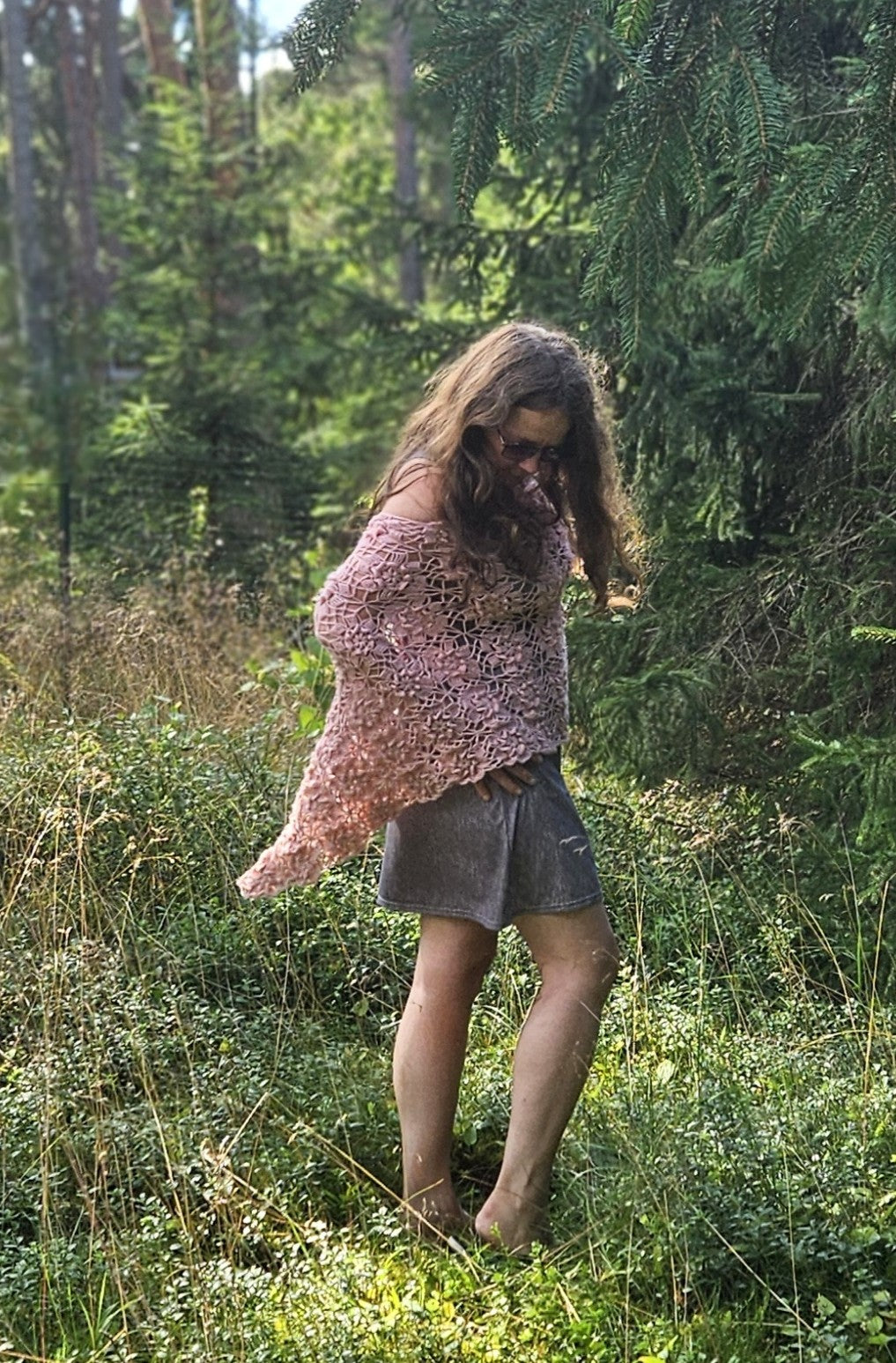 Woman in a pink crochet sakura poncho standing in a forest