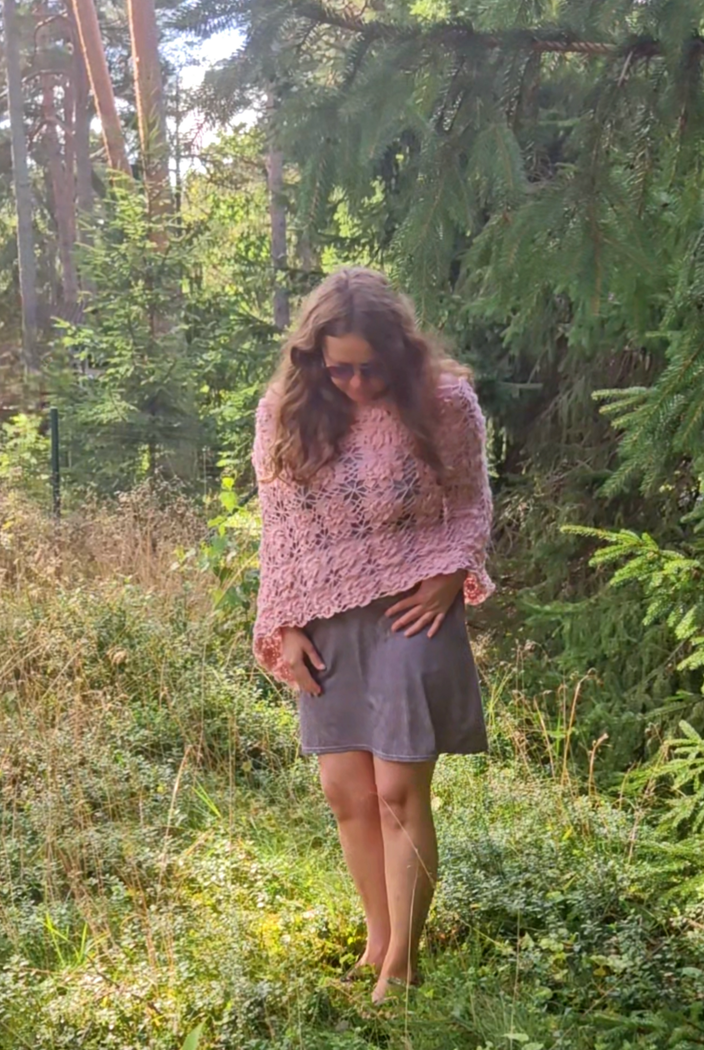 Woman wearing a pink crochet sakura poncho in a forest setting